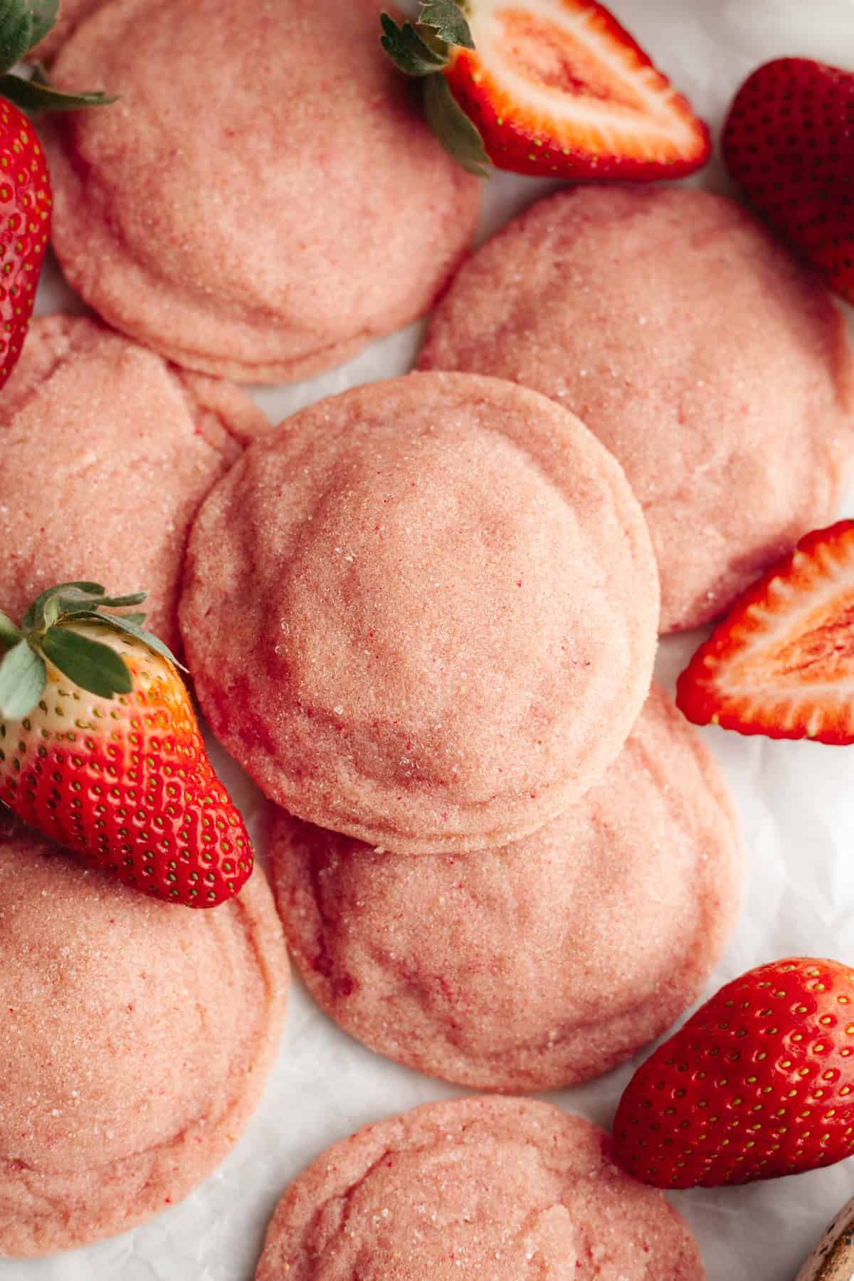 A close up of pink strawberry sugar cookies on parchment paper with fresh strawberries.