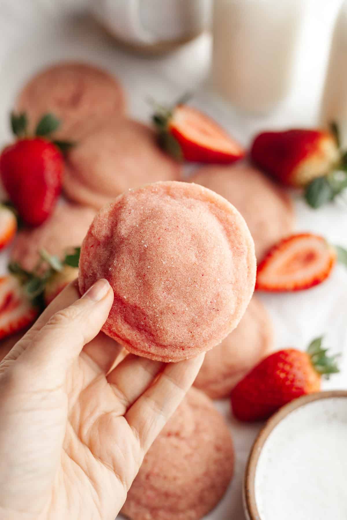 A hand holding a pink strawberry sugar cookie.