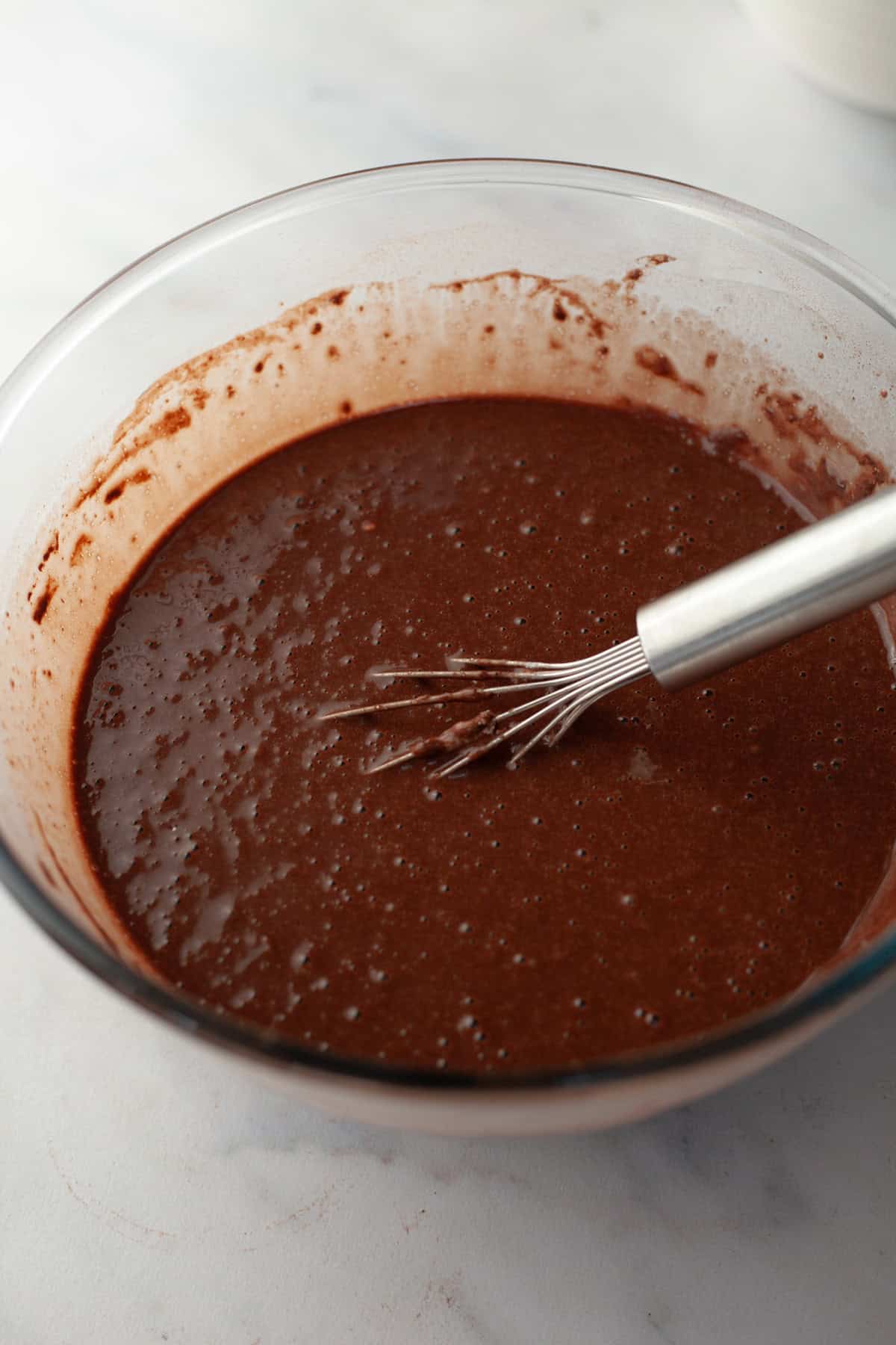 Chocolate cake batter in a glass bowl with a whisk.