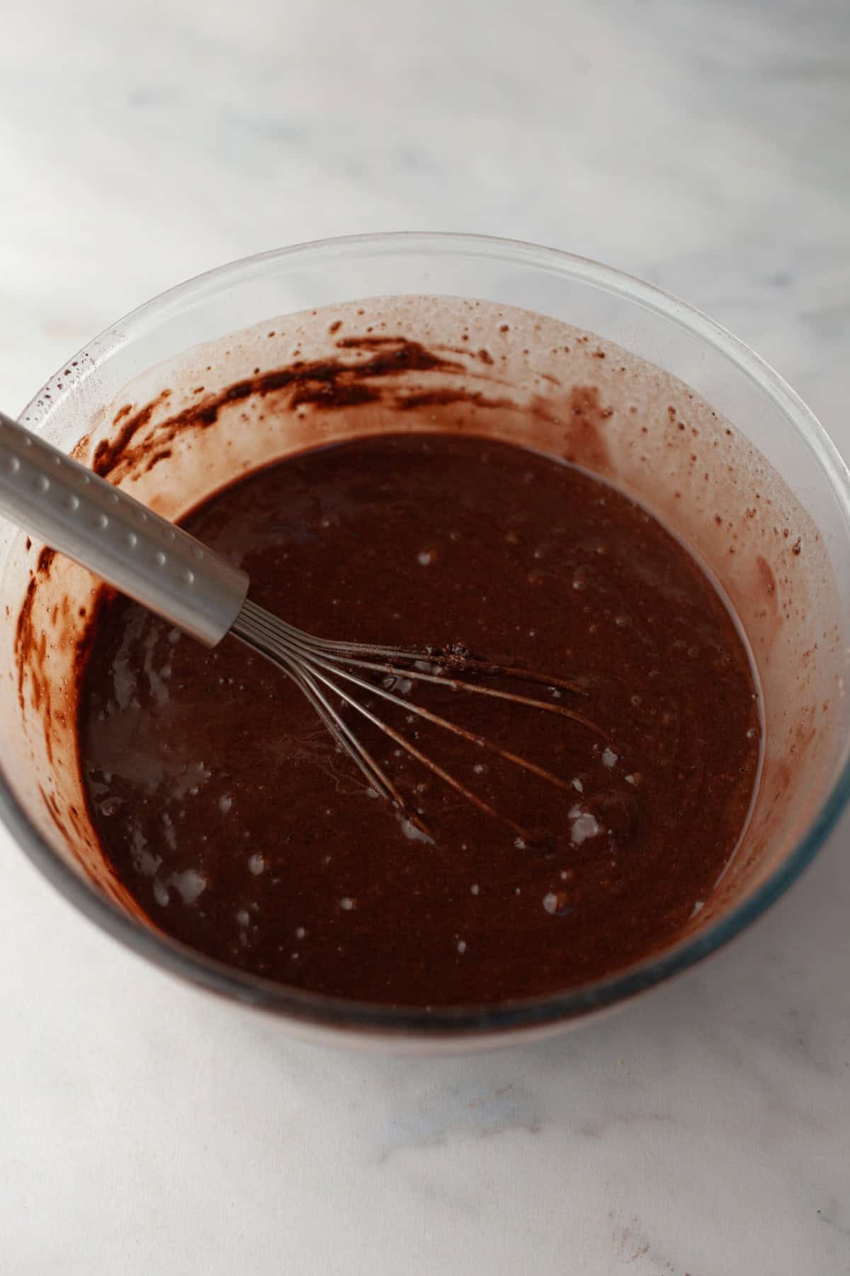 Chocolate cupcake batter in a glass bowl with a whisk.