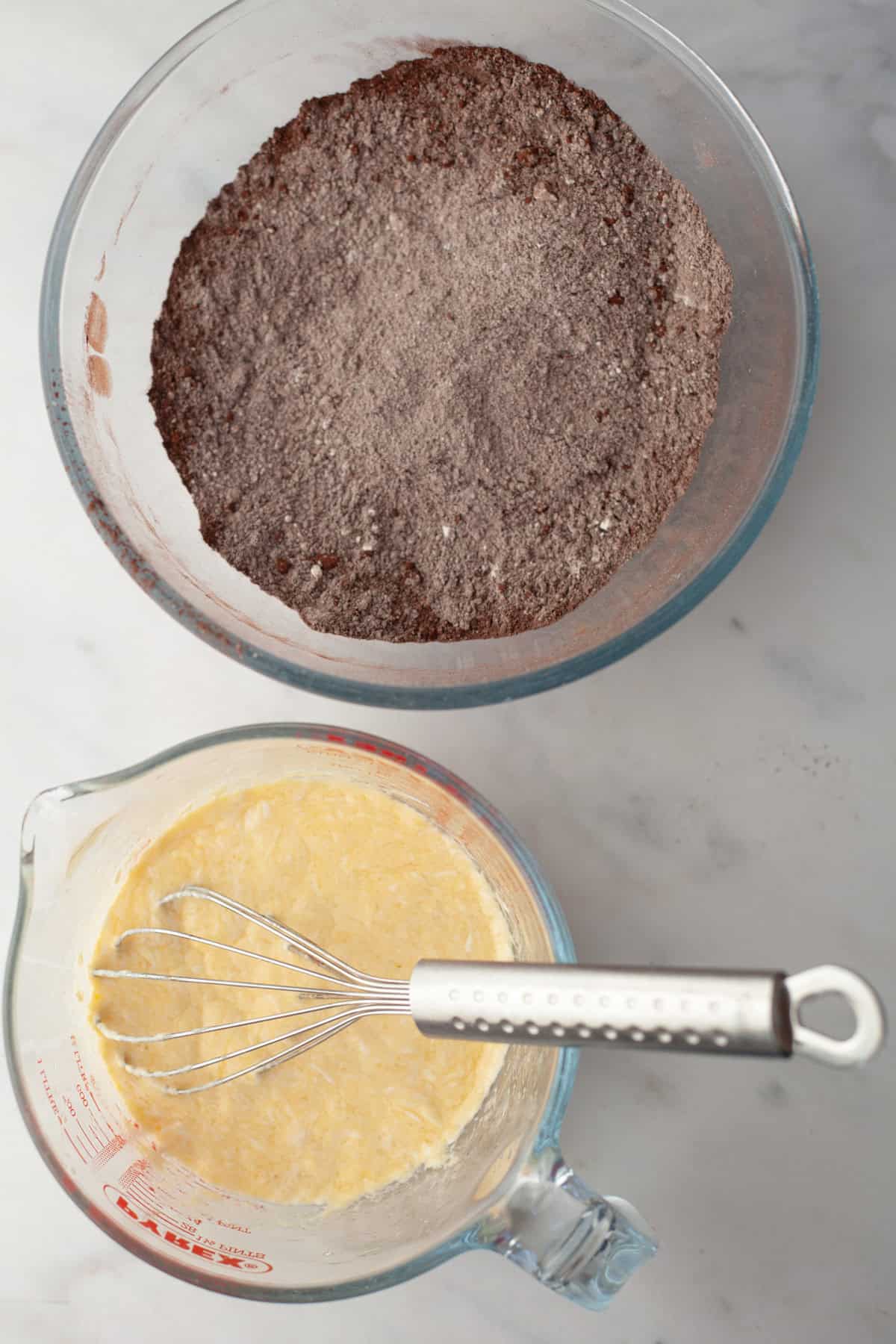 A glass bowl with cocoa powder and flour and a glass jug with a pale yellow mixture in it.