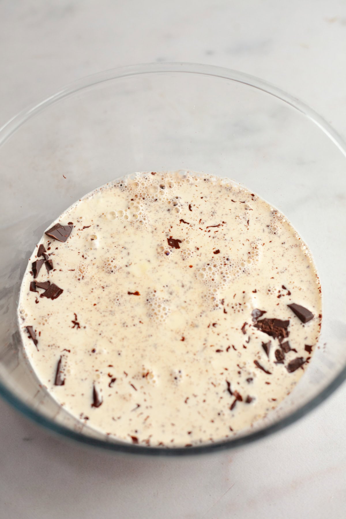 A glass bowl with cream and chopped chocolate.