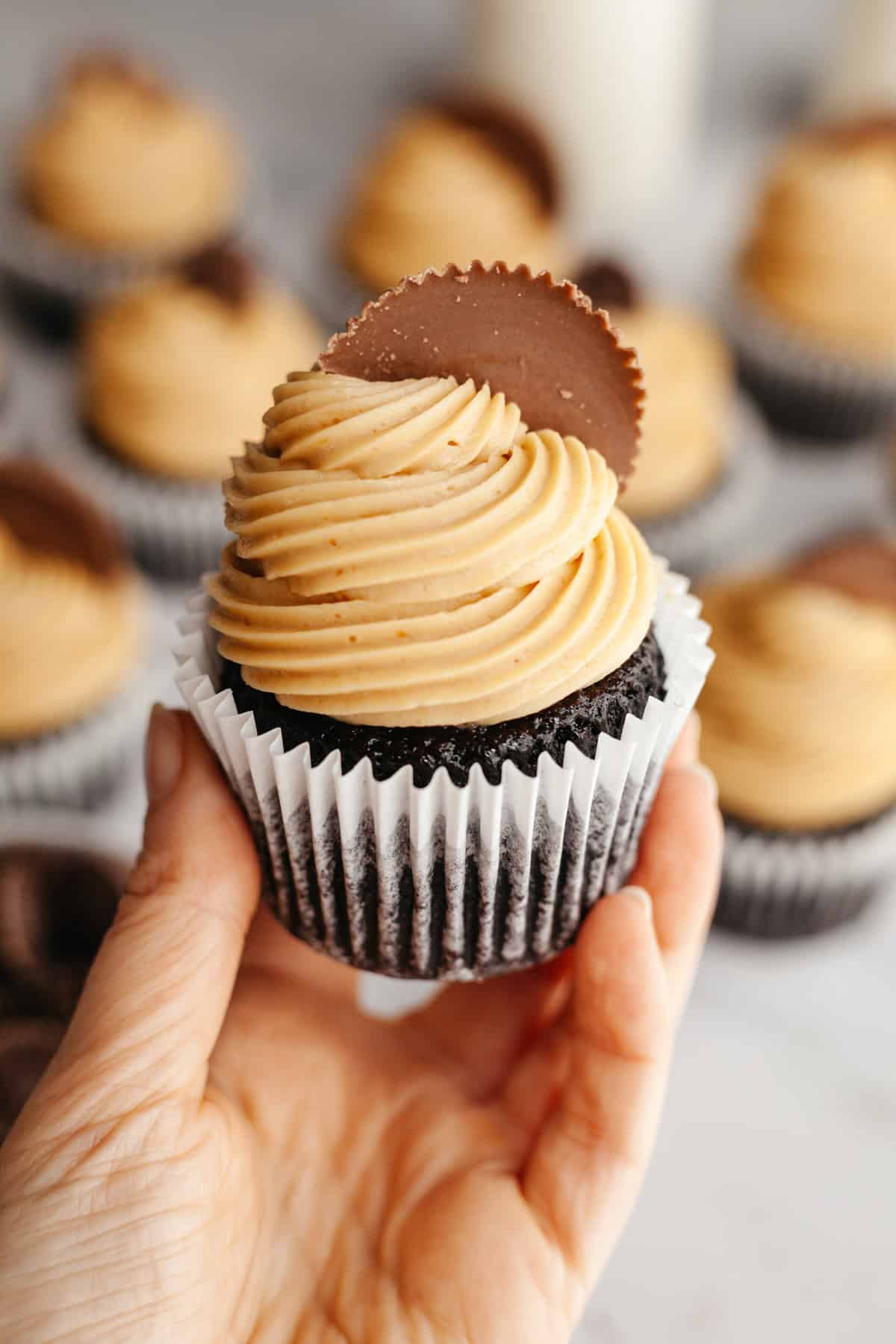 A hand holding a chocolate peanut butter cupcake with a Reese's cup on it.