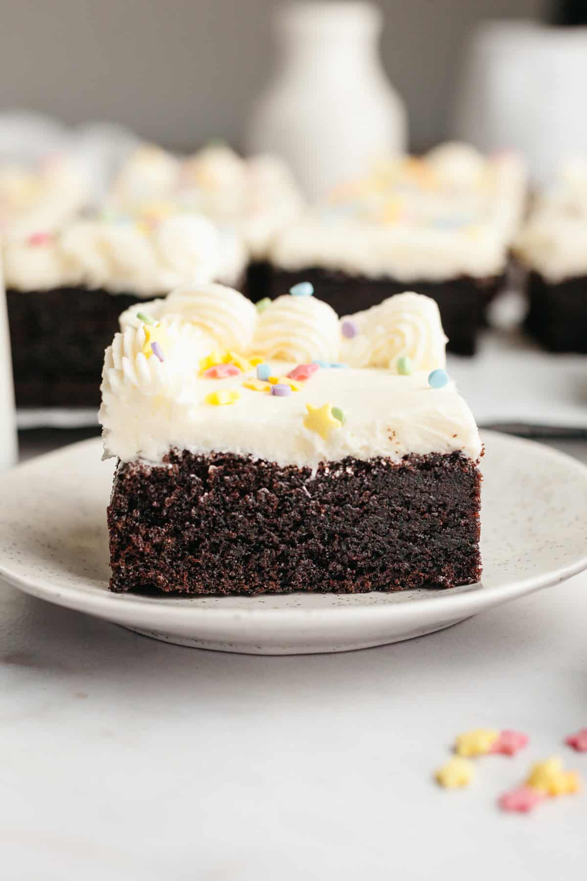 A slice of moist chocolate sheet cake with vanilla frosting on a small plate.