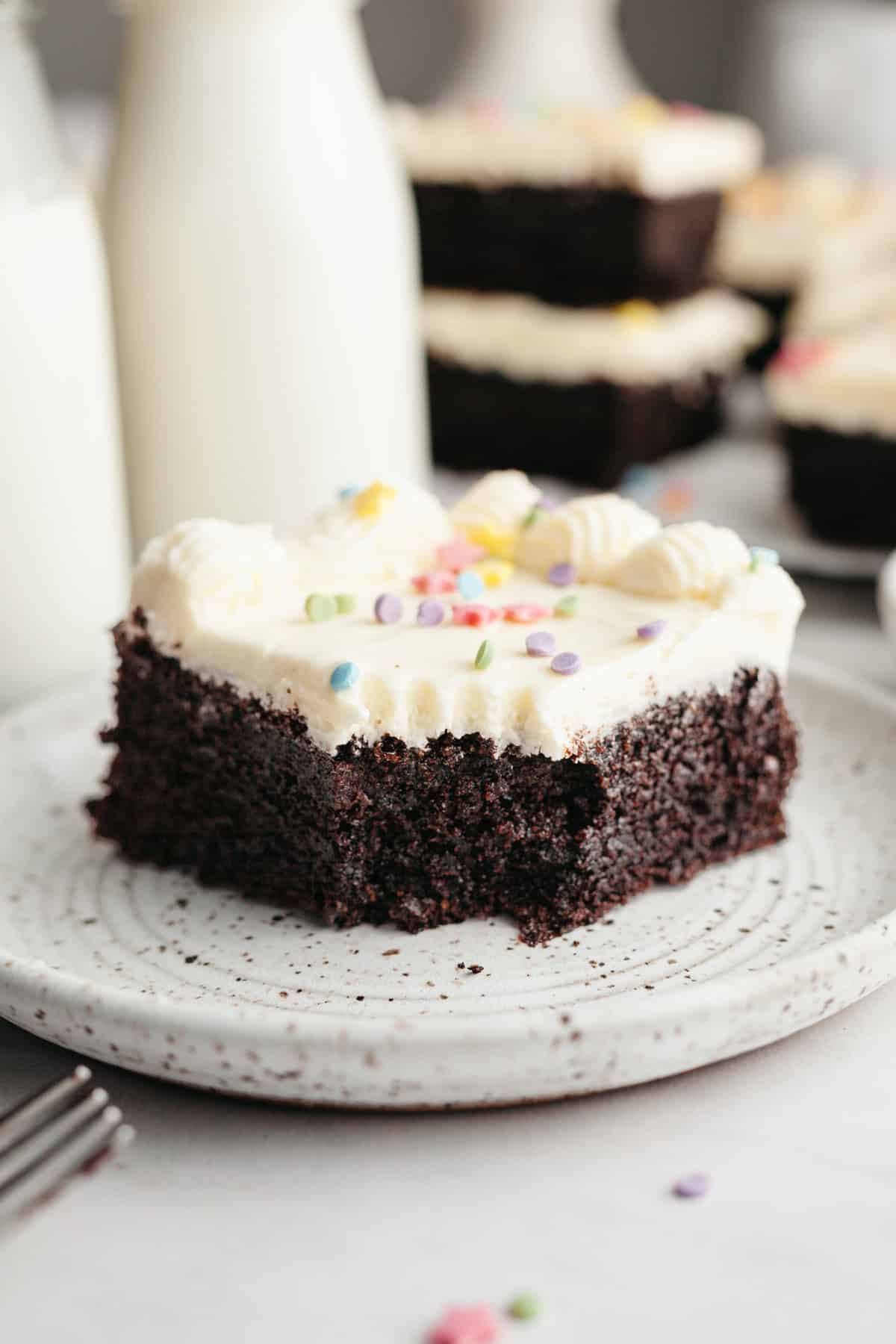 A slice of moist chocolate sheet cake with vanilla frosting on a small plate.