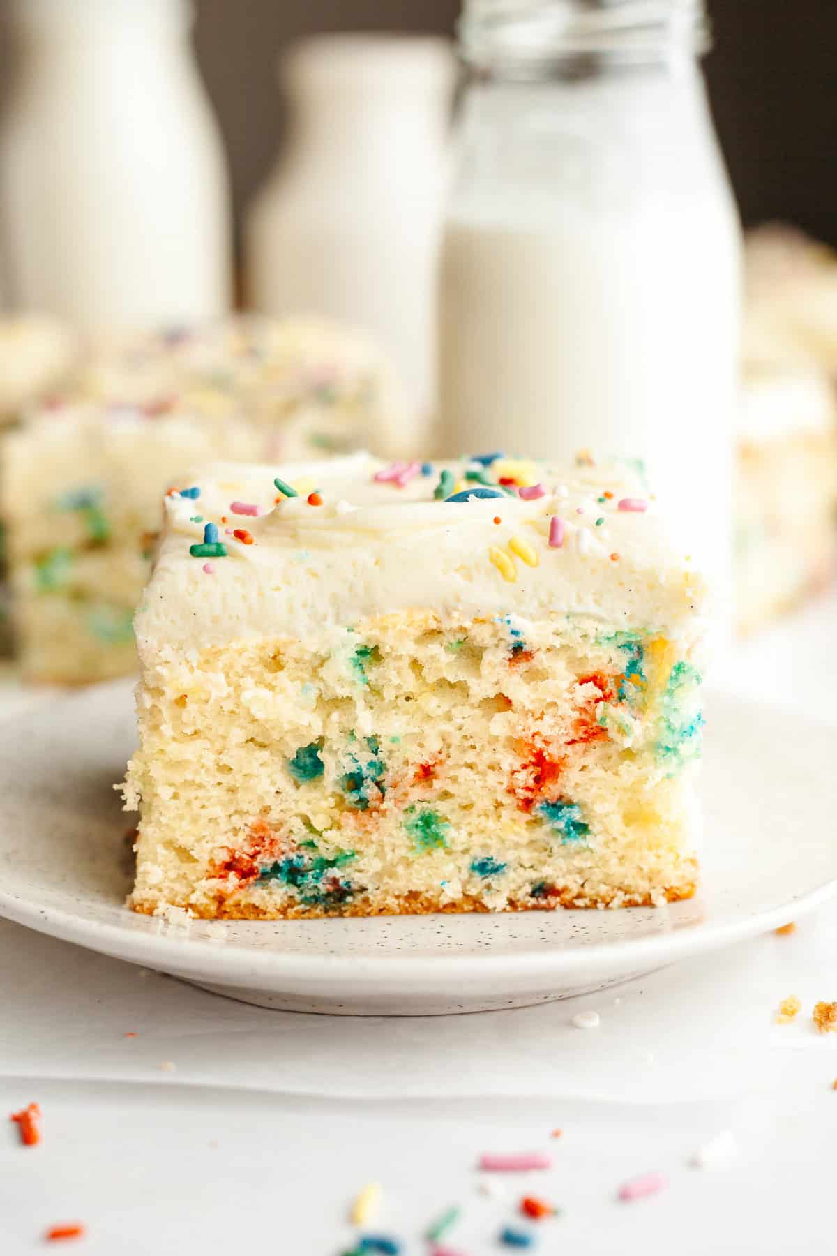 A slice of confetti sheet cake with vanilla frosting on a small plate.