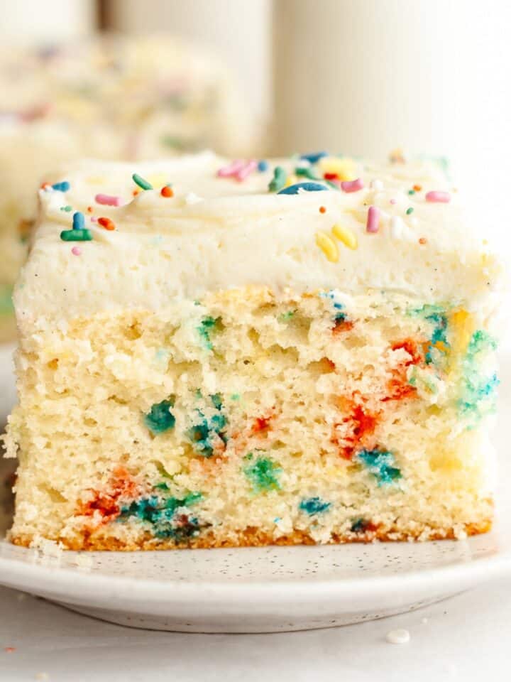 A slice of confetti sheet cake with vanilla frosting on a small plate.