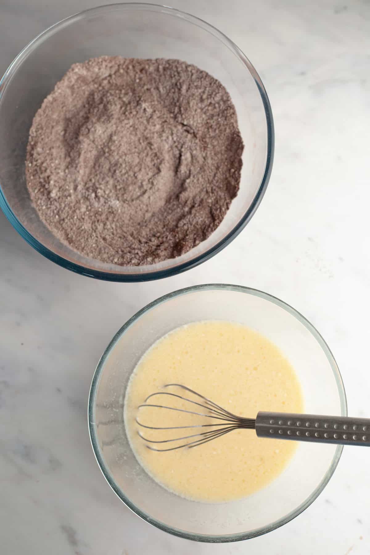 Flour and cocoa powder in a bowl, and a pale yellow mixture in a bowl with a whisk.