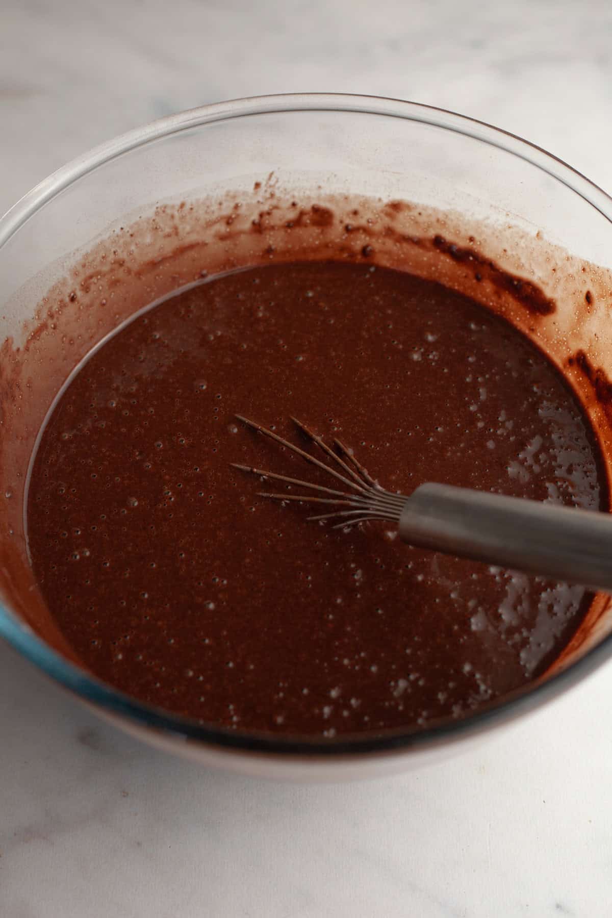 Chocolate cake batter in a glass bowl with a whisk.