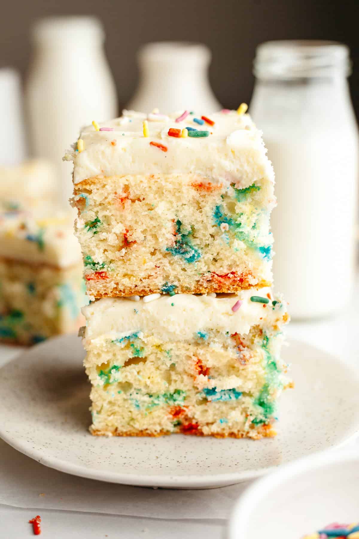Two slices of funfetti sheet cake stacked on top of each other on a small plate.