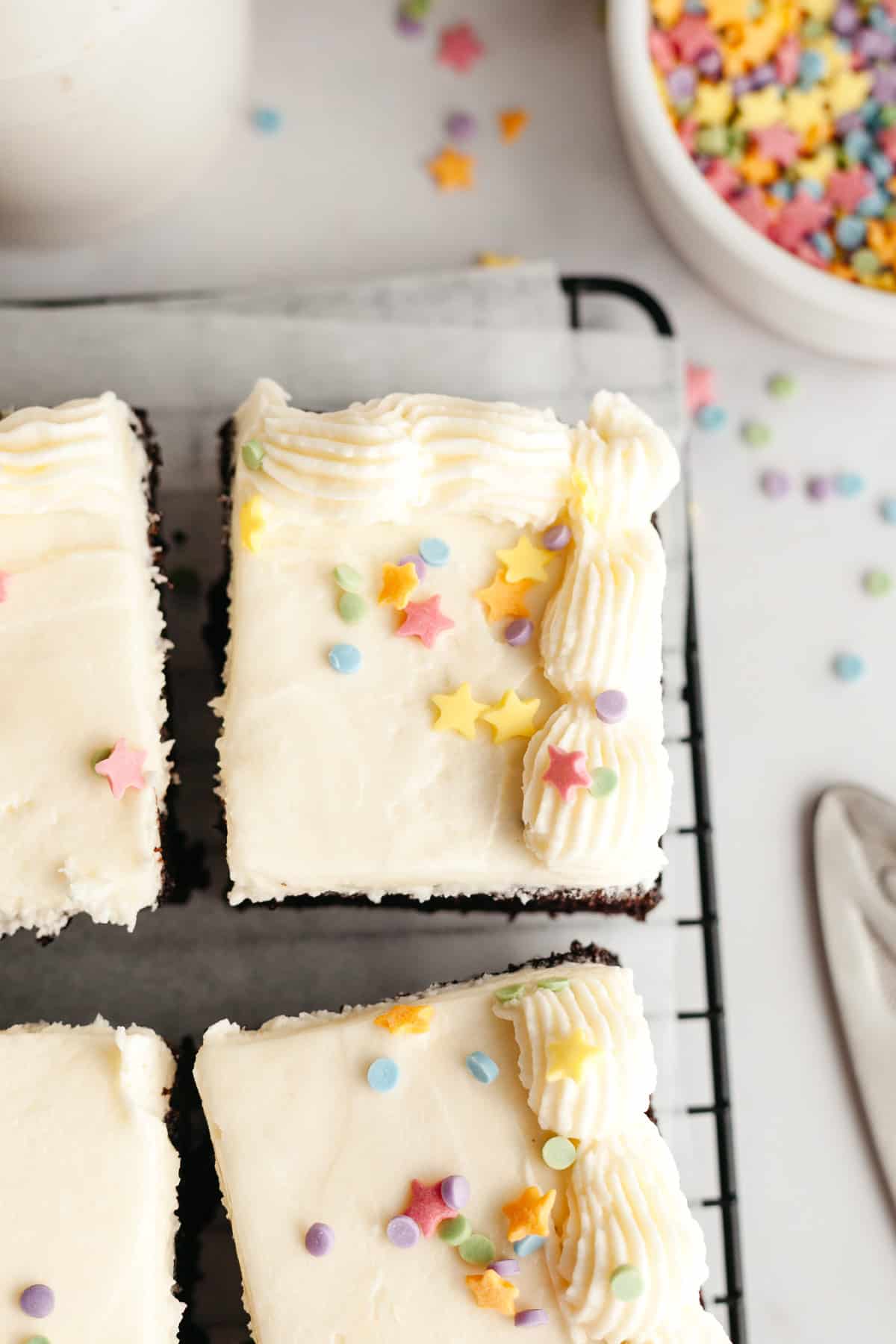 Square slices of chocolate cake with vanilla frosting and rainbow sprinkles.