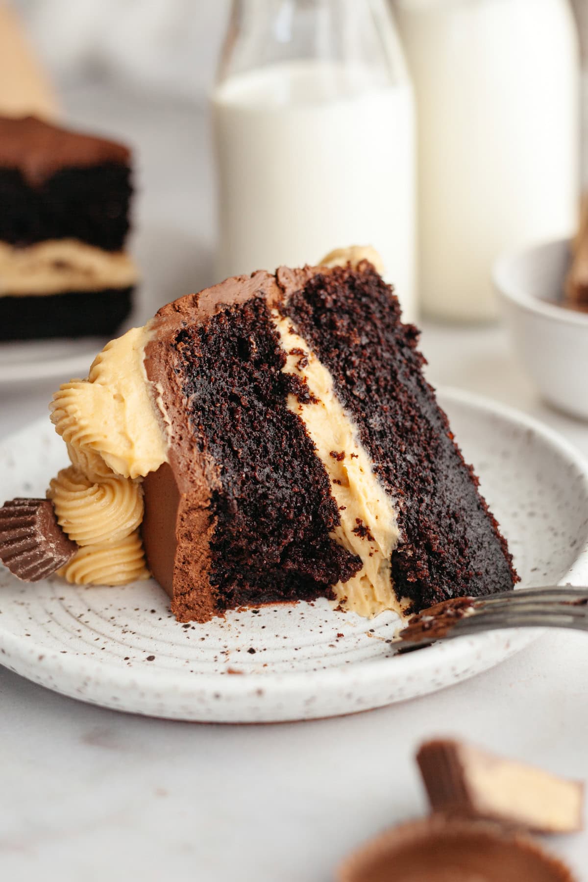 A slice of peanut butter chocolate cake on a small plate with a bite taken out of the cake.