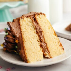 A slice of vanilla cake with chocolate frosting on a small plate.