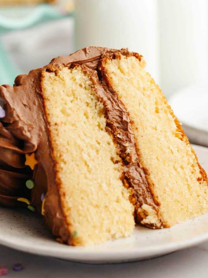 A slice of vanilla cake with chocolate frosting on a small plate.