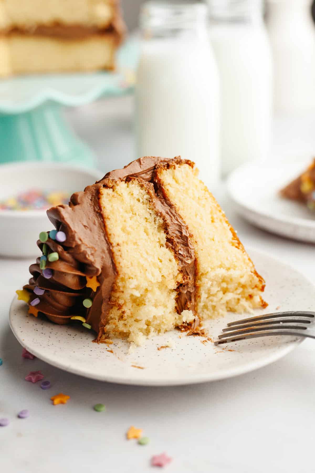A slice of vanilla cake with chocolate frosting on a small plate.