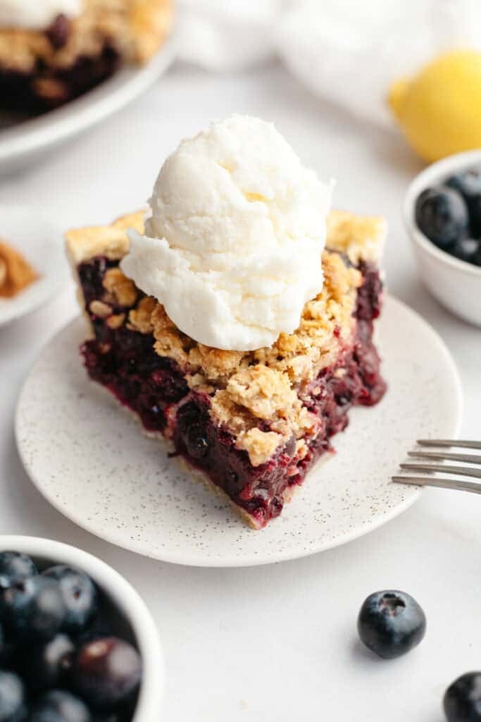 A slice of blueberry crumb pie with a large scoop of vanilla ice cream.