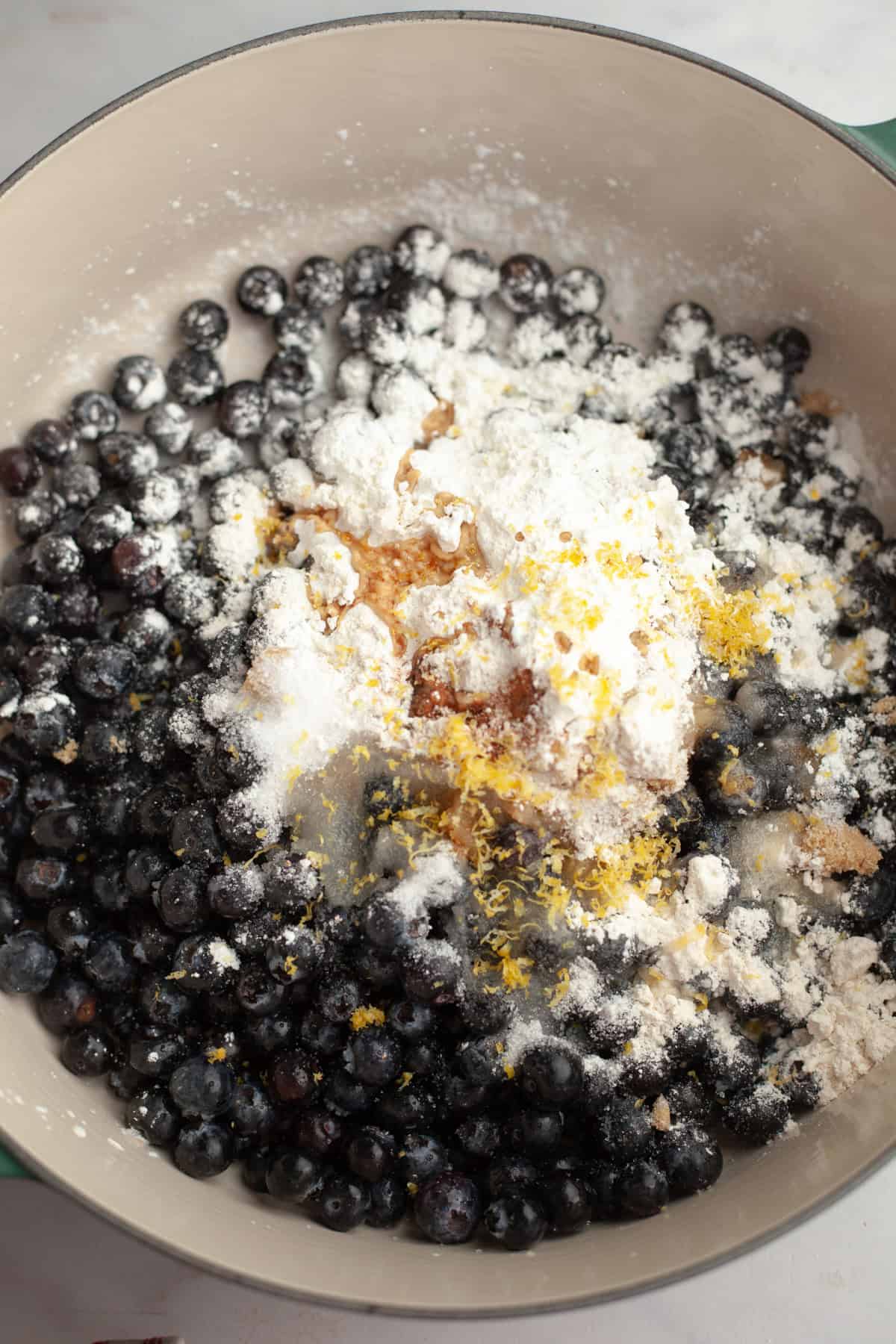 A dutch oven with fresh blueberries, lemon zest, sugar, and cornstarch.