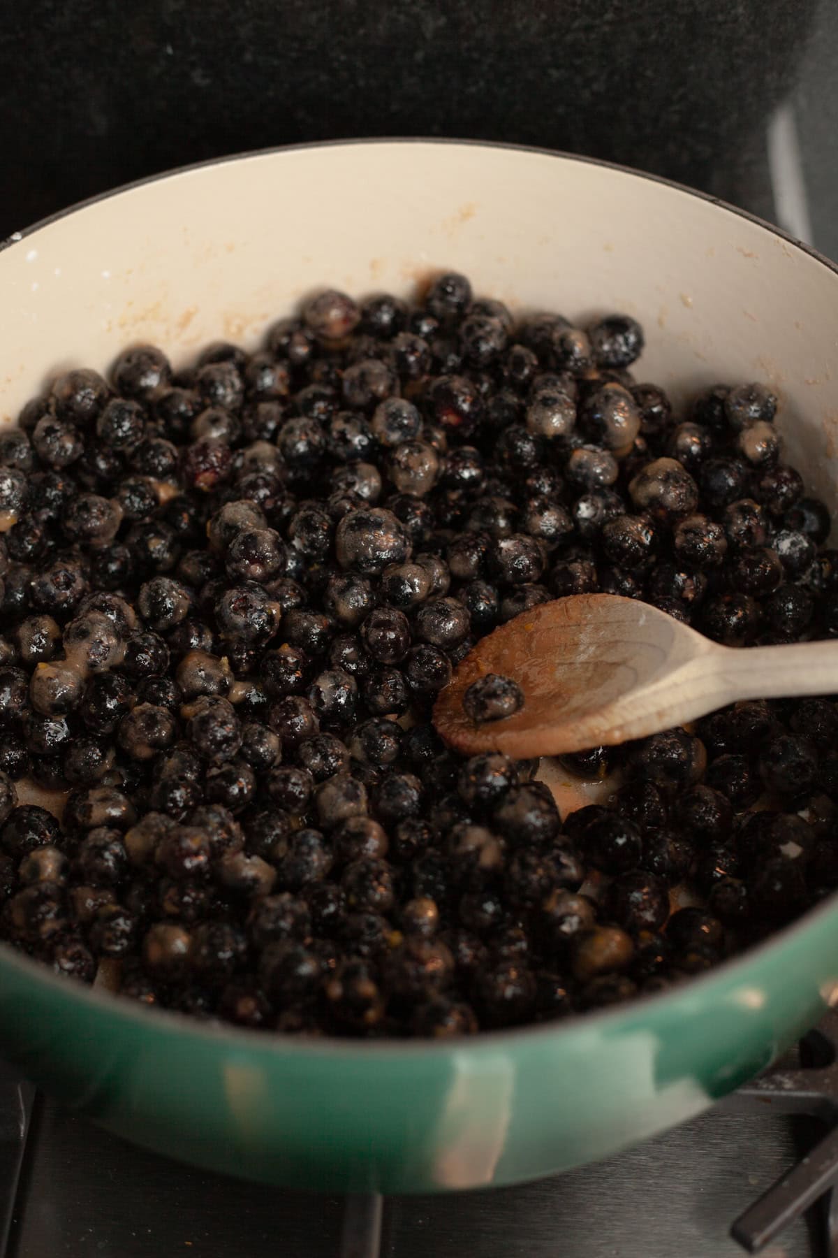 A dutch oven with blueberry pie filling and a wooden spoon.