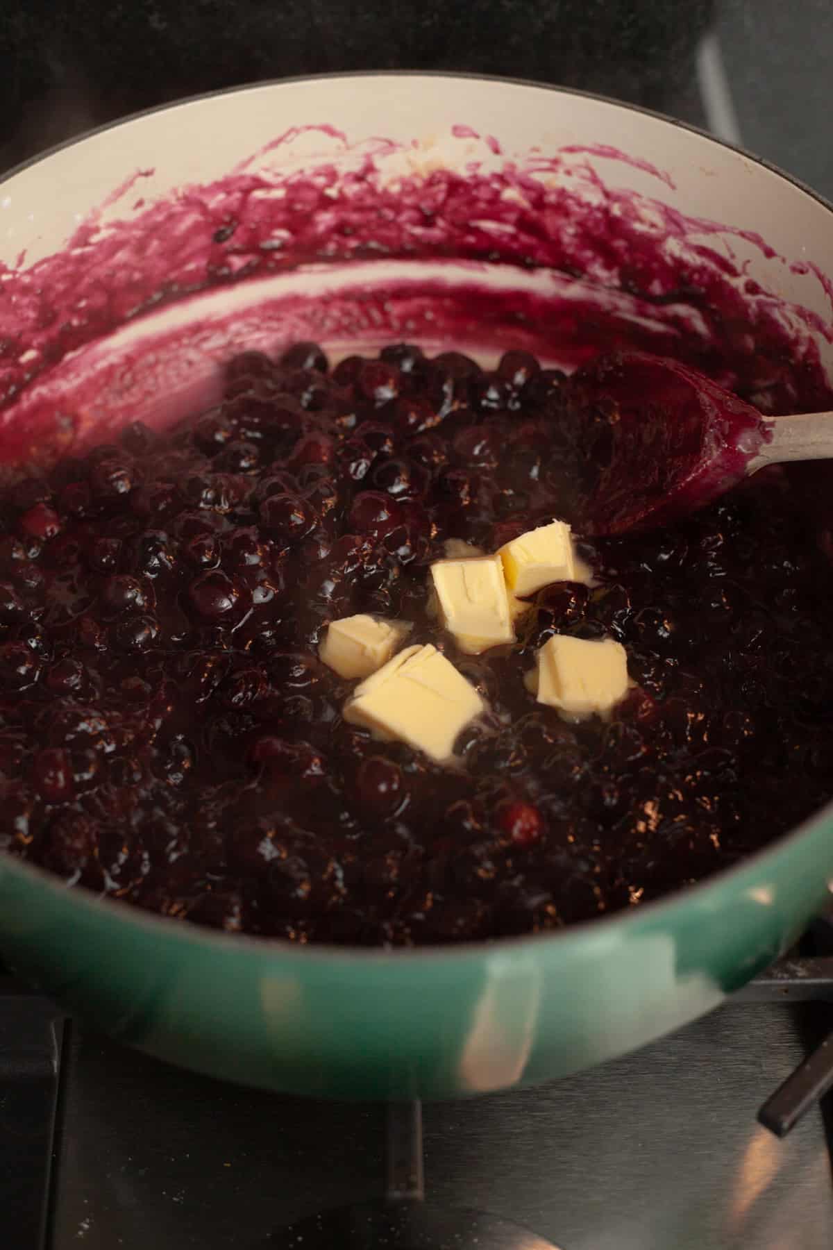 A dutch oven with blueberry pie filling and pieces of butter.