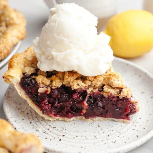 A slice of blueberry crumb pie with a large scoop of vanilla ice cream.