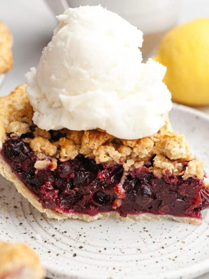 A slice of blueberry crumb pie with a large scoop of vanilla ice cream.