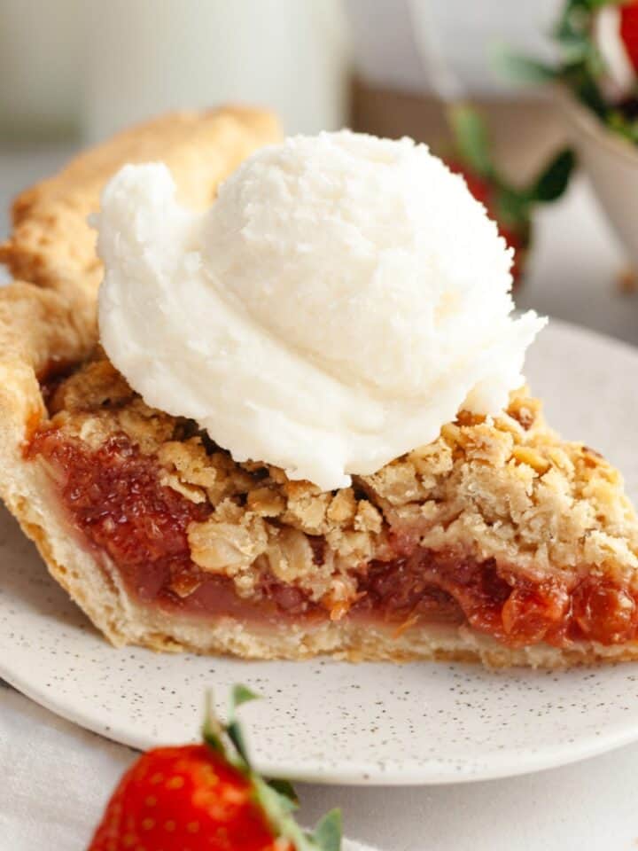 A slice of strawberry rhubarb pie with a scoop of vanilla ice cream.