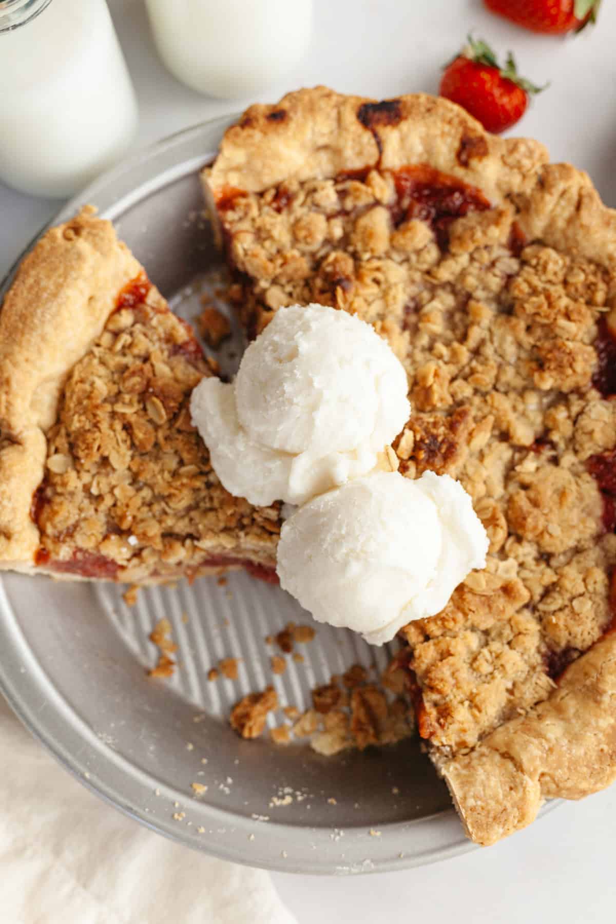 An overhead shot of strawberry rhubarb pie, several slices have been cut and there are two scoops of vanilla ice cream.