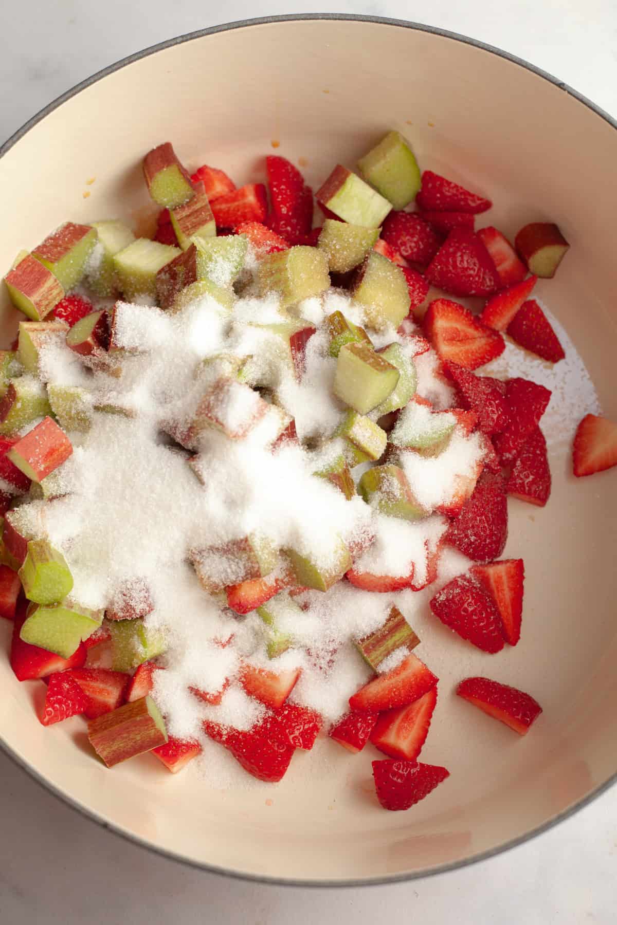 A large dutch oven with chopped strawberries, rhubarb, and sugar.