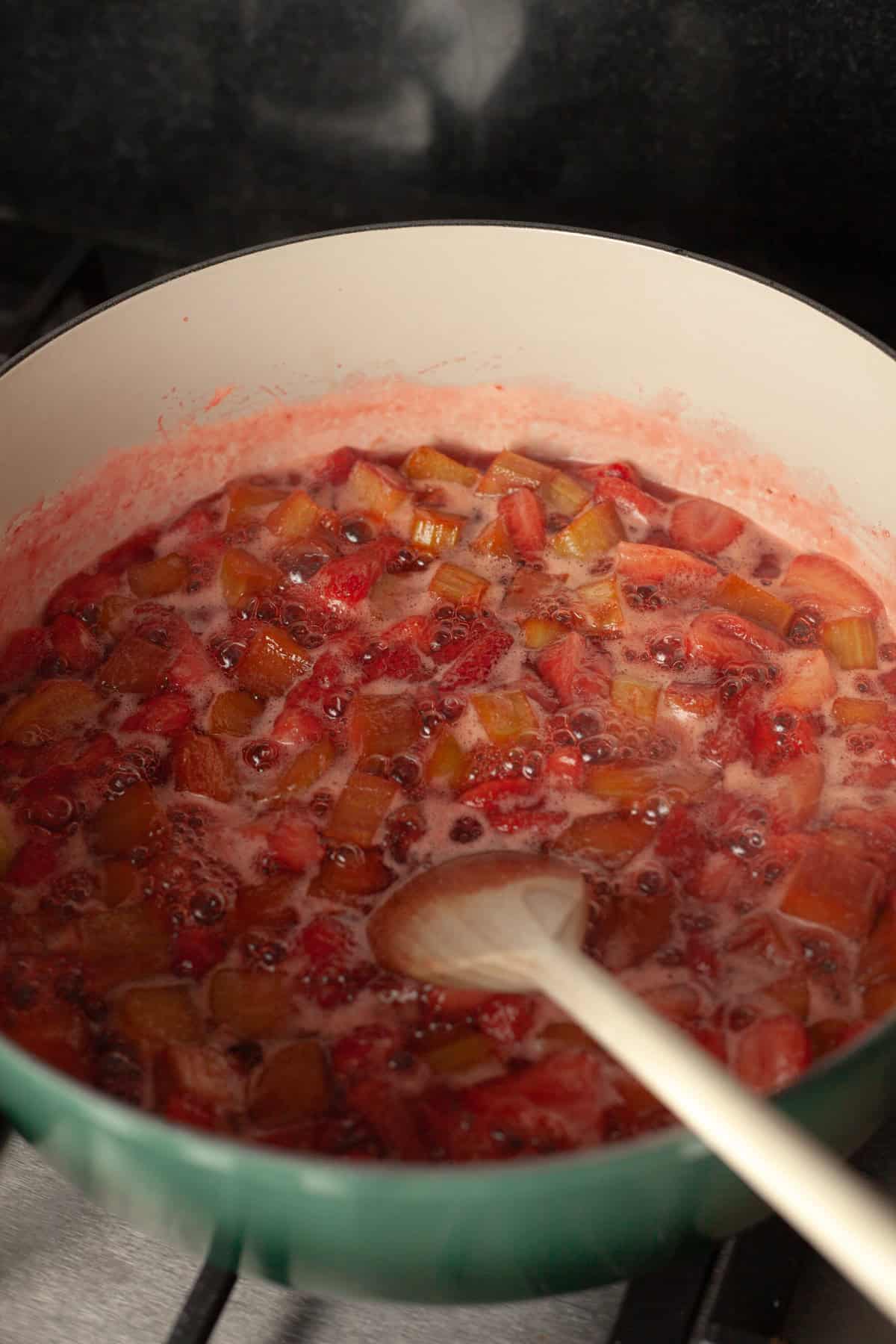 A shallow dutch oven with strawberry rhubarb pie filling bubbling inside.