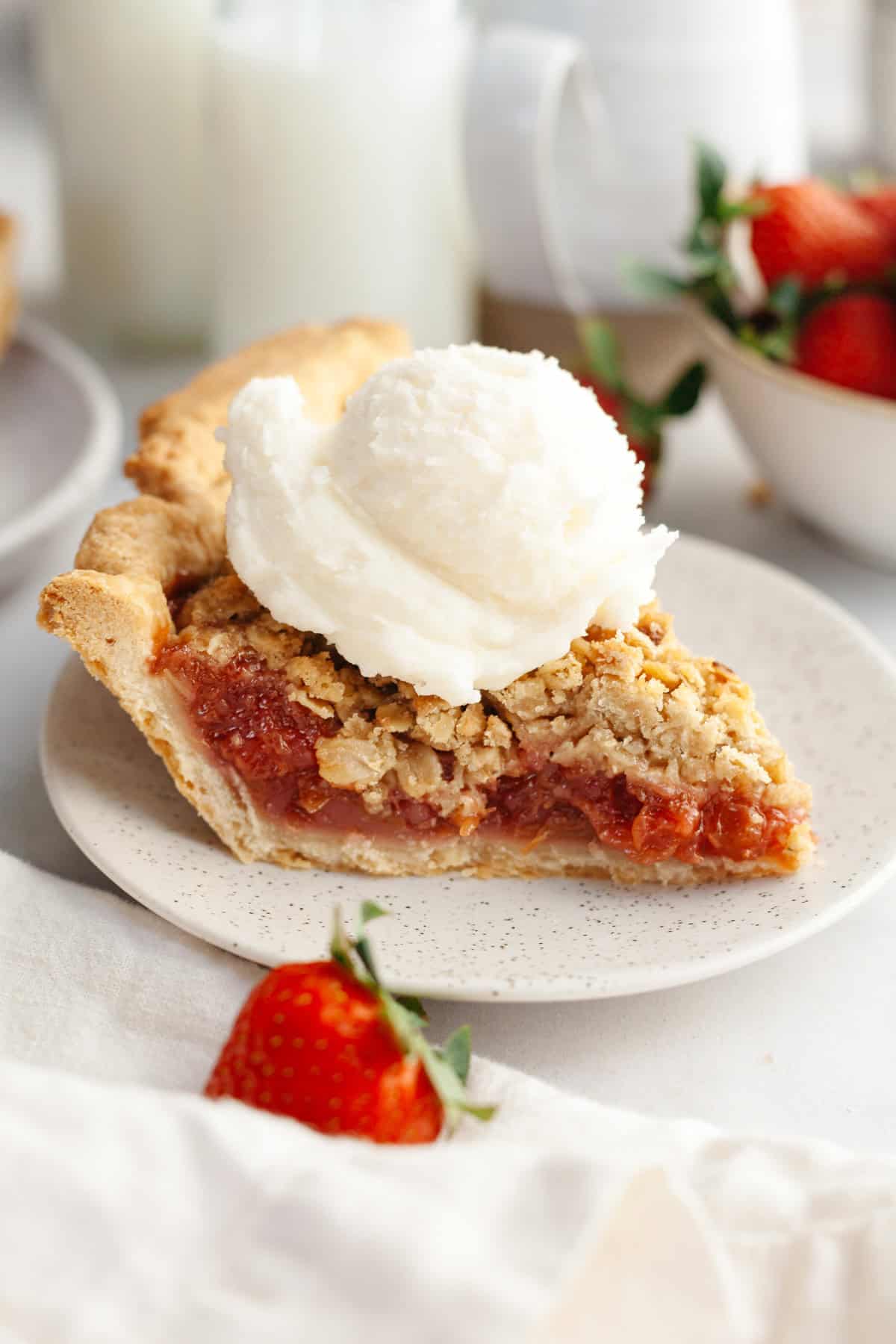 A slice of strawberry rhubarb pie with a scoop of vanilla ice cream.
