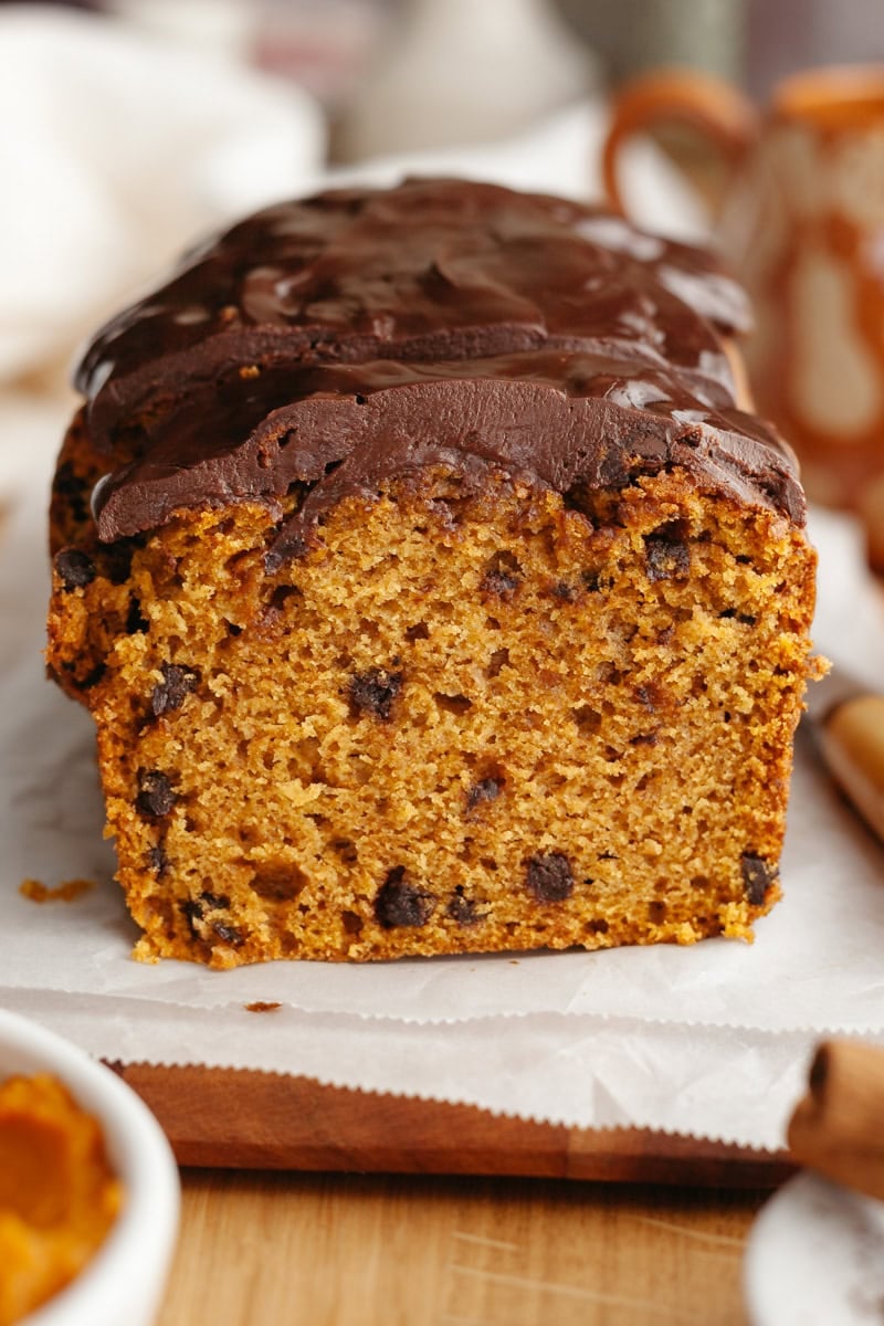 A sliced pumpkin chocolate chip loaf with a glossy chocolate glaze, displayed on a wooden board.