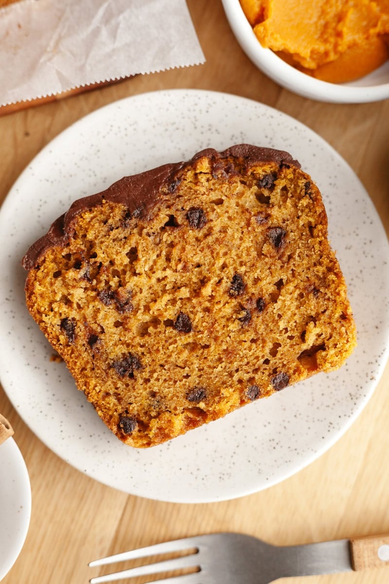 A close-up of a slice of chocolate chip pumpkin loaf cake on a white plate, showing its moist texture and chocolate chips.