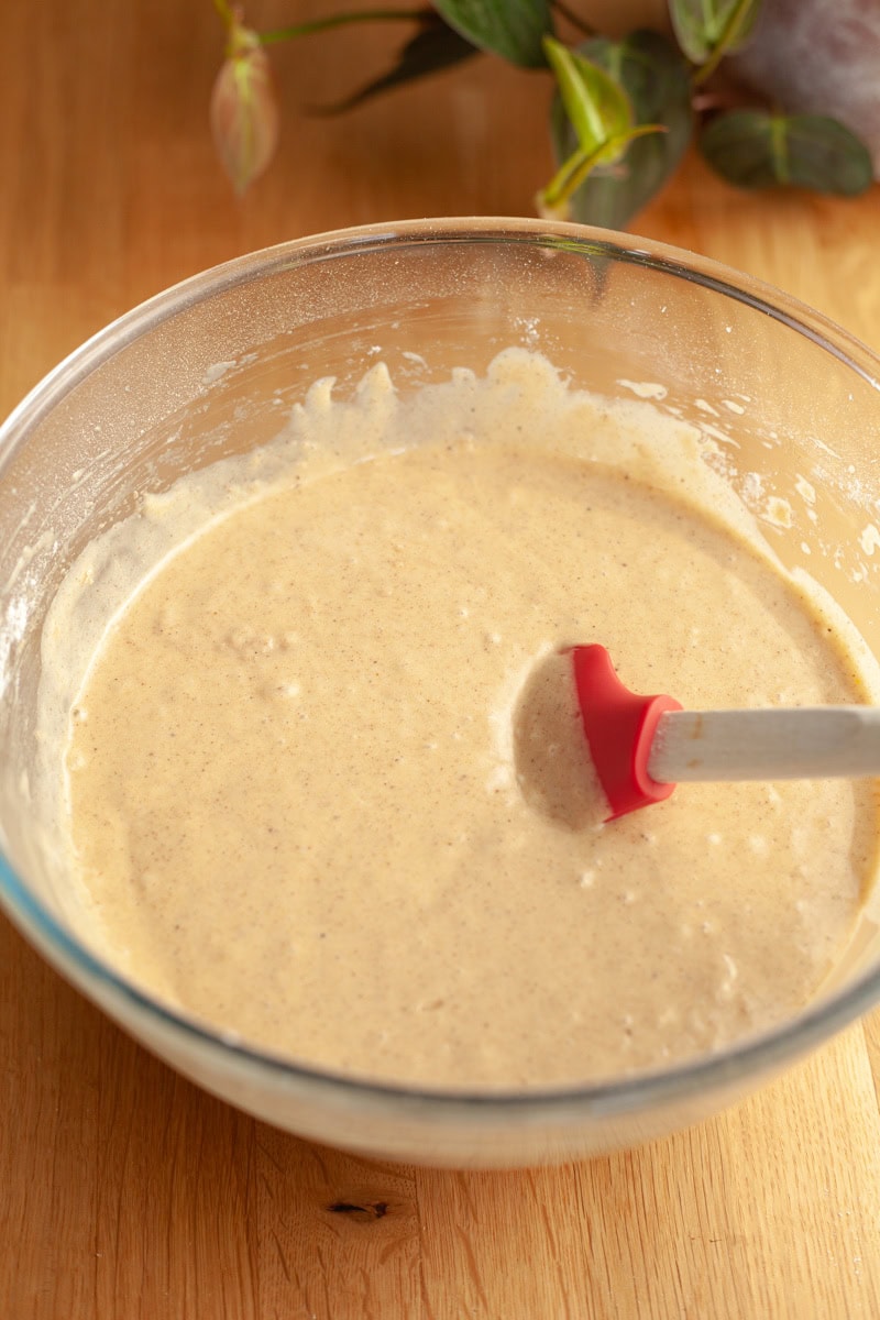 Apple cake batter in a glass bowl with a rubber spatula.