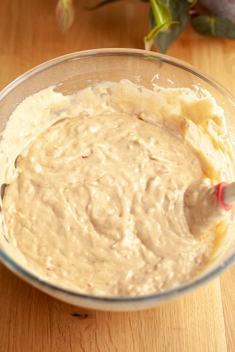 Apple cake batter in a glass bowl with a rubber spatula.
