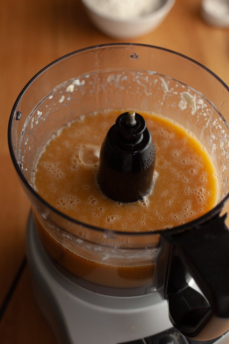 A food processor with a light brown cake batter in it.