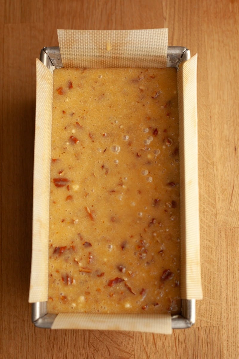 A loaf pan filled with unbaked pecan loaf cake batter.