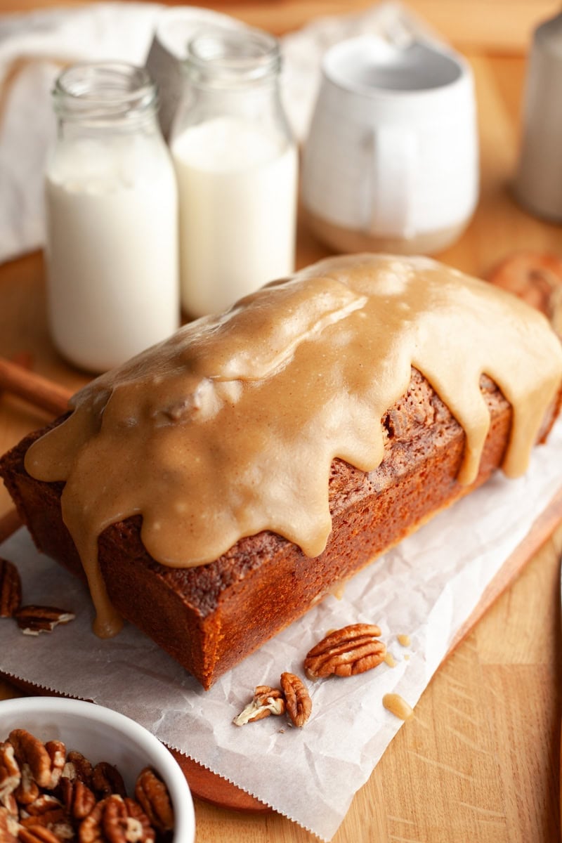 A butter pecan loaf cake covered in a caramel glaze, the loaf is on parchment paper.