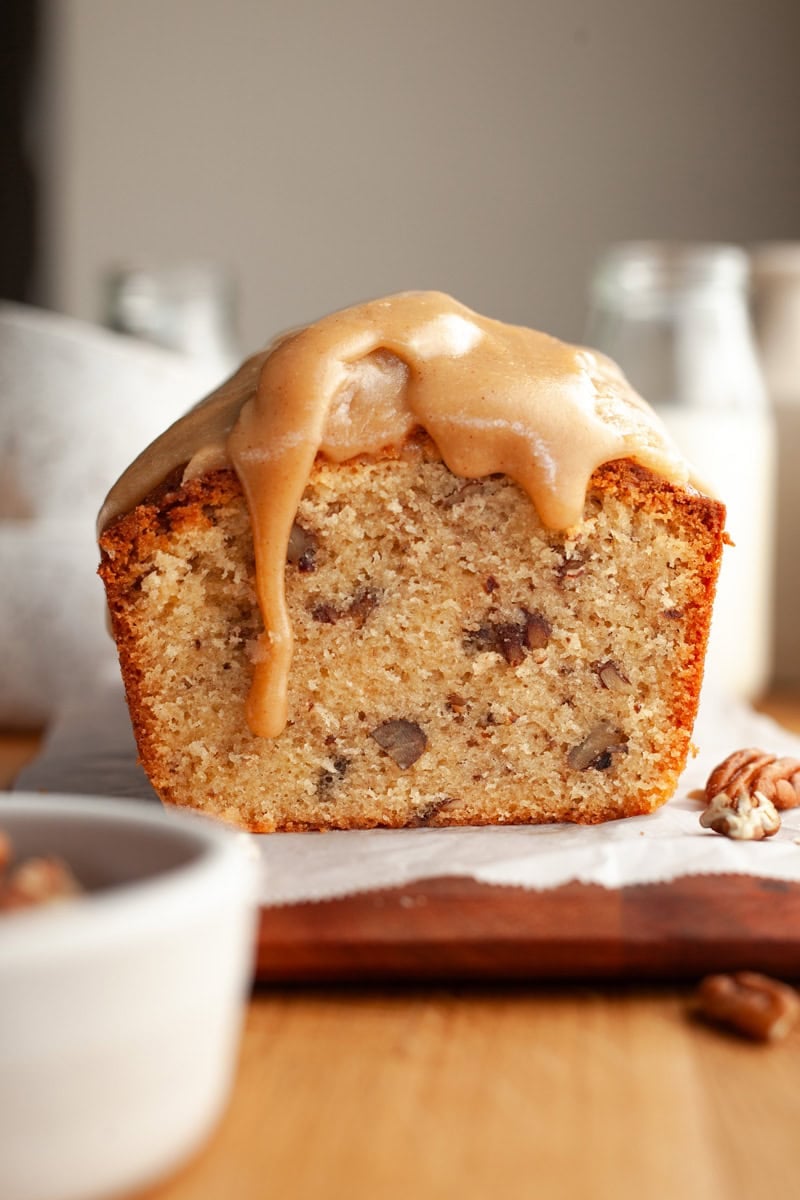 A pecan loaf cake sliced with a caramel glaze dripping down.