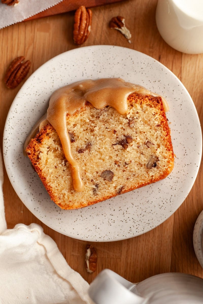 A pecan loaf cake slice with a caramel glaze dripping down on a small plate.