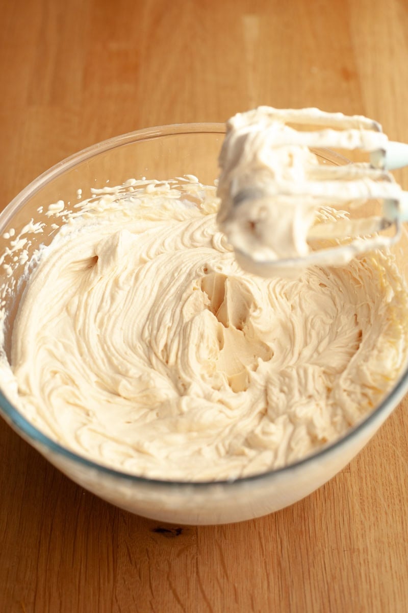 A mixing bowl filled with whipped salted caramel cream cheese frosting, with a hand mixer coated in the frosting resting in the bowl.
