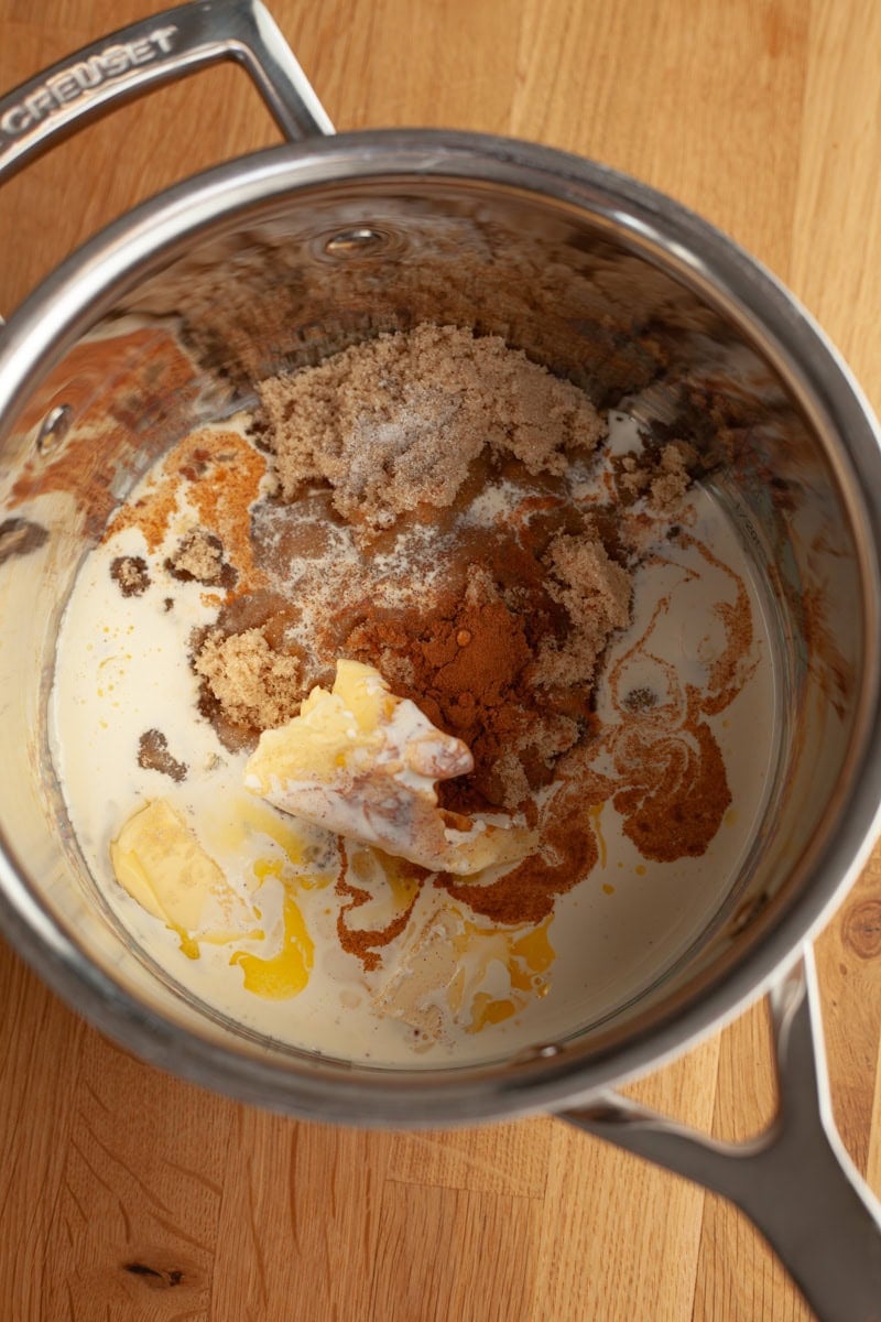 A silver saucepan with cream, butter, cinnamon, and brown sugar in it.