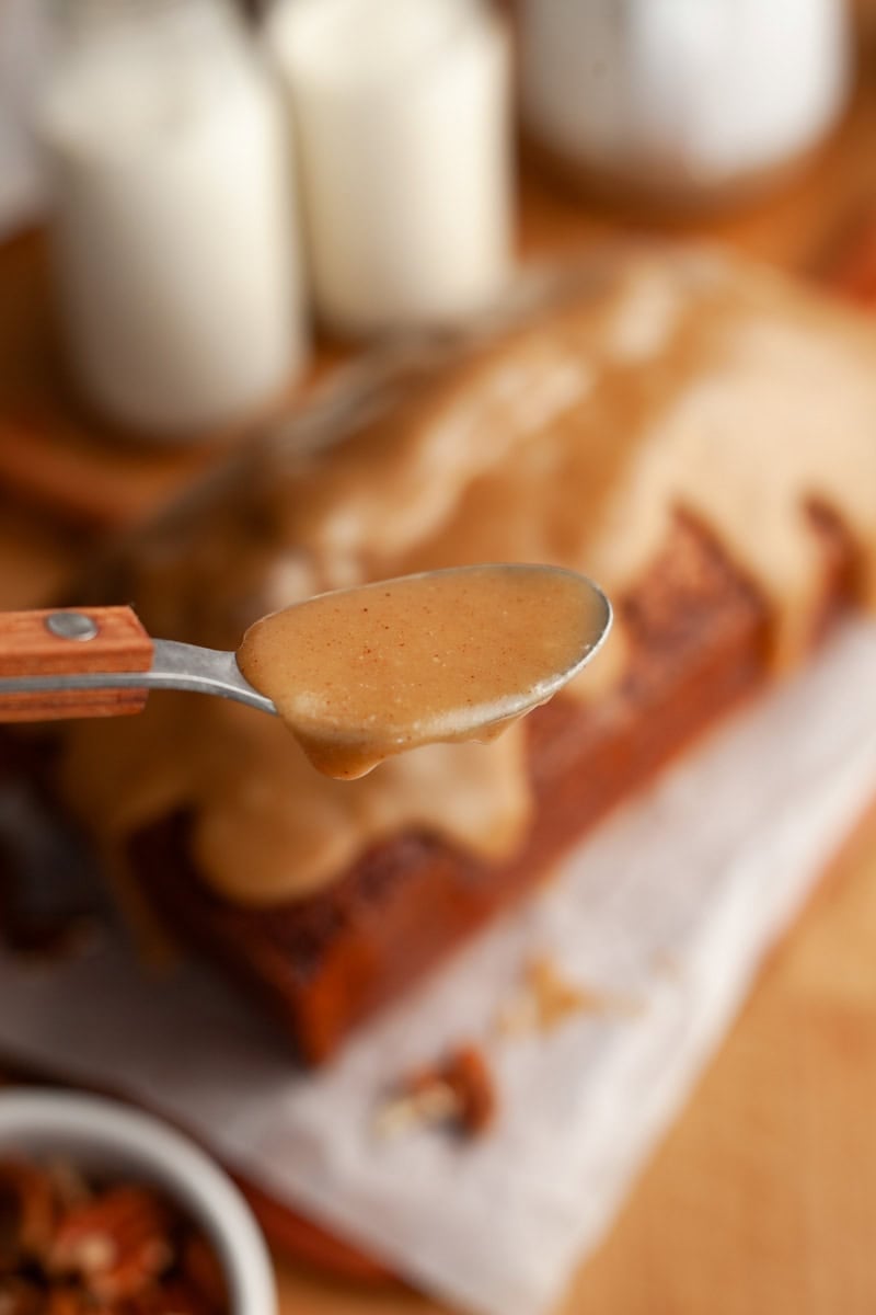 A spoonful of light brown glaze, you can see a glazed pound cake is in the background.