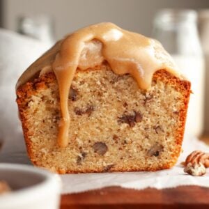 A butter pecan loaf cake sliced on parchment paper with a caramel glaze dripping down.