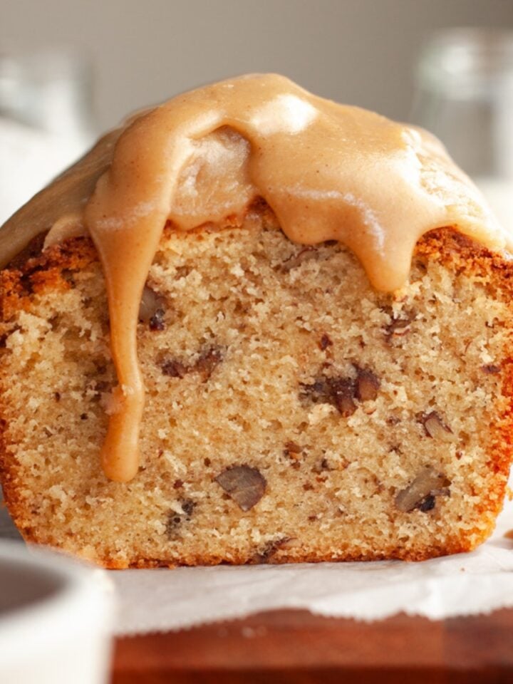 A butter pecan loaf cake sliced on parchment paper with a caramel glaze dripping down.