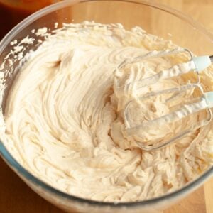 A mixing bowl filled with whipped salted caramel cream cheese frosting, with a hand mixer coated in the cream resting in the bowl.