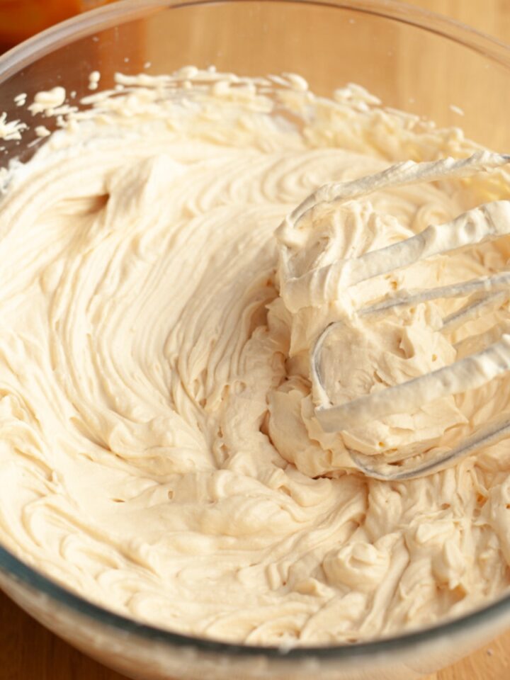 A mixing bowl filled with whipped salted caramel cream cheese frosting, with a hand mixer coated in the cream resting in the bowl.