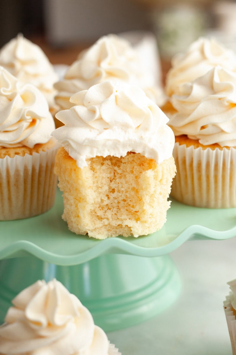 Brown butter cupcakes on a turquoise cake stand, one has a bite taken out of it.