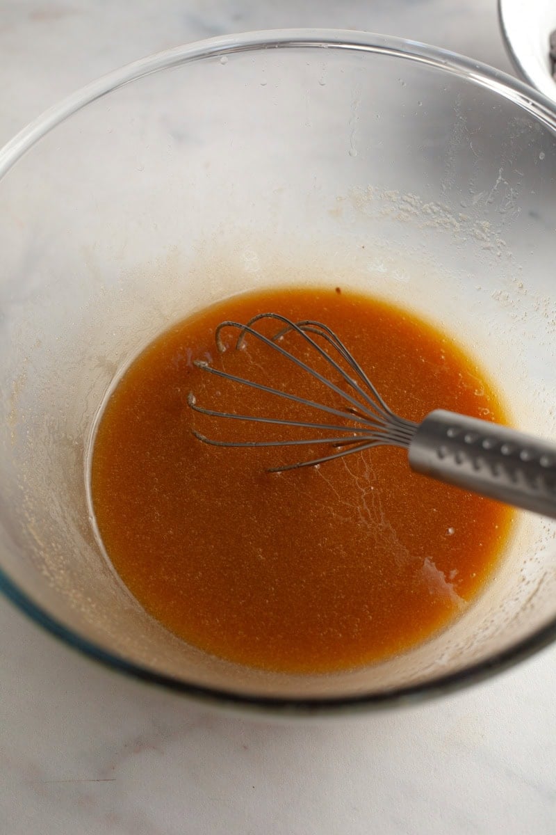 A glass bowl and a silver whisk with a light brown mixture inside.