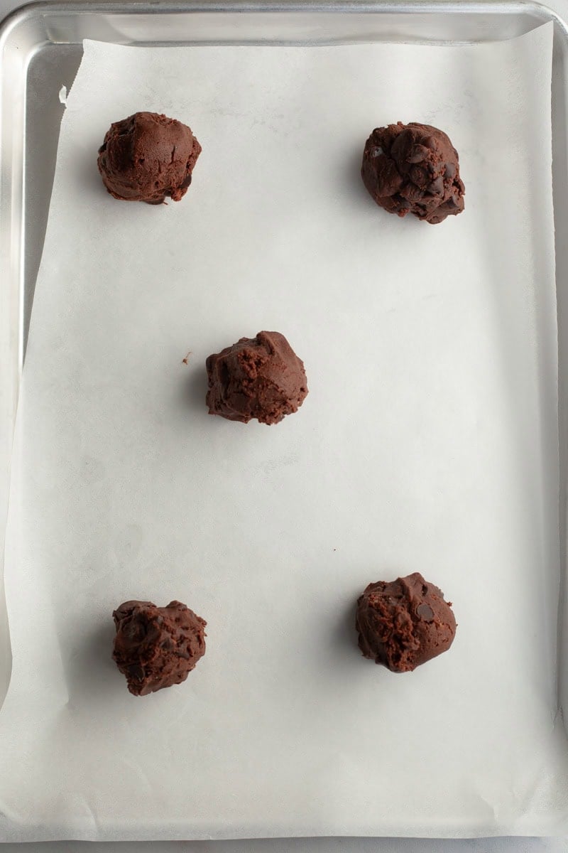 Five chocolate cookie dough balls on parchment paper.