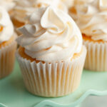 A yellow cupcake with white frosting on a teal cake stand.